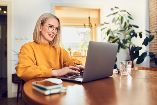 A smiling woman sits in front of a laptop. She is typing.